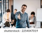 A happy businessman introducing himself while standing at the office with coworkers in blurry background.