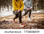 Close up of shape fitness girl in sportswear doing leg stretching with her personal trainer in the forest in the sunny winter morning.