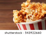 Caramel popcorn in striped box on wooden background