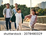 happy asian family with two children walking on pedestrian bridge in city park