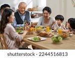 Small photo of young asian woman sharing pictures in cellphone with three generation family while eating meal together
