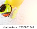 anti noise headphones, eye protection goggles, reflective vest, worker's uniform on background of architectural drawings, health protection at work