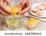 Woman hands breaking an egg to separate  egg  white and  yolks and egg shells at the background  