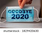 The hand holds a medical and protective mask with the word GOODBYE 2020. Concept of coronavirus quarantine. Prevent or stop the spread of the COVID-19 worldwide.