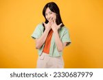 Small photo of shy asian young woman 30s covering her mouth with hands isolated on yellow background. expression of embarrassment or uncertainty. shyness, embarrassment, and body language concept.