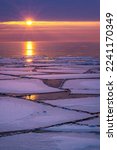 Small photo of Ice floes float on Lake Superior during a winter thaw. A rising sun breaks the horizon and cast light and reflections across the water and ice on a cold winter morning
