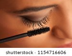 closeup of a young dark-skinned woman applying mascara on a white background