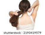 Rear view of a young woman tying her long hair on a white background.