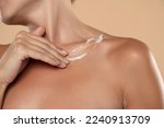 Small photo of Woman apply body cream lotion on her chest on a beige studio background