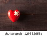 Small photo of Red broken heart with a band-aid on a wooden background