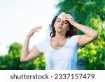 Small photo of Young woman having hot flash and sweating in a warm summer day. Woman drying with paper napkin in too hot weather