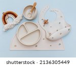 Small photo of Flat lay composition with silicone baby bib and beige dishware on blue background. Flat lay, top view