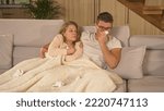 Small photo of CLOSE UP: Cute married couple in quarantine due to getting over covid-19 virus. Twosome on sick leave and resting on comfy couch at home. Young man and woman covered with blanket and recovering.