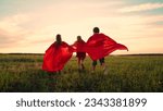 Small photo of Happy girls, boy kids play superheroes they run across green field in red cloak, cloak flutters in wind. Childrens games dreams