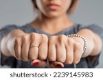Small photo of fists clenched together of a young woman. is this a sleight of hand and hiding something, or is it a threatening gesture? In any case, she is wearing a ring and a bracelet, and her nails are painted r