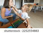 Small photo of Side view of the game mom and daughter play in the living room: the little one puts makeup on her and she pretends to be ticklish in the nose