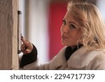Small photo of Young woman huffs bored and flippant as intercom rings. Does she do door-to-door sales or did she forget her keys at home?