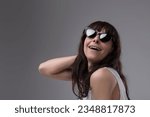 Small photo of perfectly ordinary woman feels alluring, stylish, and beautiful just by wearing sunglasses. She strikes a stereotypical pose of haughty cinema divas, feigning a wide-open laugh. Concept of vanity. Hea