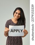 Small photo of The call to 'APPLY' is presented by a woman whose warm eyes and gentle smile amplify the invitation. Her patterned top provides a soft backdrop to the straightforward directive