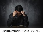Asian man reading book or bible hand over head having stressful depression sad time sitting on the table. Depression man sad serios reading book. Education learning bible religion concept.