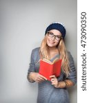 Small photo of Happy student girl with book in hands wearing stylish hat and glasses isolated on gray background, enrollee of university