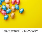 Easter chocolate eggs wrapped in aluminium foil on the yellow background. Top view.