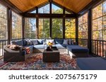 Small photo of Cozy screened porch with contemporary furniture and flower bouquet in a vase, autumn leaves and woods in the background.