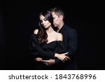 Small photo of beautiful woman in evening dress in the hands of man in a suit. Couple over black background. Adorable, elegant girl seducing her handsome boyfriend