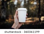 female hand holding a blank paper cup with plastic cap in a autumn forest background