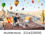 Happy couple on a rooftop in Cappadocia with hot air balloons in the background. Hot air balloon flights in Turkey