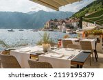 Street view of a outdoor waterfront terrace with tables and chairs in restaurant in Perast historic village in Kotor Bay, Montenegro. Summer vacation destination concept