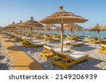 Beautiful empty beach with sun umbrellas and sunbeds. Perfect summer vacation destination. Straw sunshades and sunbeds on the empty beach with blue sea on background