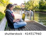 Young woman using laptop at a riverbank.