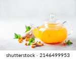 Hot autumn tea with sea buckthorn, ginger and mint in a glass teapot on a gray background