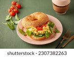 Small photo of Bagel with scramble eggs, lettuce and tomatoes in a plate on a green background. Breakfast idea