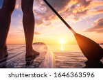 Stand up paddle boarding or standup paddleboarding on quiet sea at sunset with beautiful colors during warm summer beach vacation holiday, active woman, close-up of water surface, legs and board