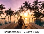 Woman relaxing by the pool in a luxurious beachfront hotel resort at sunset enjoying perfect beach holiday vacation