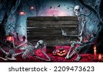 Small photo of Halloween Card In Forest With Wooden Sign Board - Graveyard At Night With Pumpkins And Skeletons