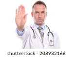 Small photo of Doctor or male nurse wearing a lab coat holding up his hand in a stop gesture with a stern implacable expression as he prevents access or tells people to halt or go away, isolated on white