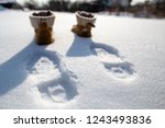 Footprints and shoes on pure white snow on a cold sunny day, in the blurry background.
