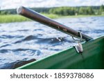 Small photo of Metal oarlock holding an oar in a boat, against the background of a lake on a summer day.