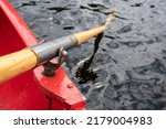 Small photo of Oar is held on an oarlock attached to a red boat, against the background of water.