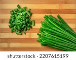 Stems and chopped pieces of fresh green onions on striped wooden kitchen board. Juicy chopped green scallion or chives slices and stalks. Greenery, seasoning for cooking fresh healthy salad. Close up.