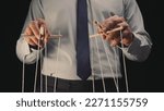 Small photo of A businessman in a gray shirt and black tie controls a puppet with a wooden manipulator and strings. The puppeteer manipulates the puppet by pulling the ropes with both hands. Close up.