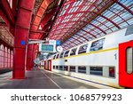 Antwerp, Belgium. Central indoor railway station. Platform made of red metal constructions with clock and panel with departure or arrival schedule. Modern double decker high-speed train.