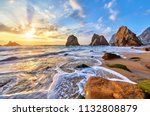 Portugal Ursa Beach at atlantic coast of Atlantic Ocean with rocks and sunset sun waves and foam at sand of coastline picturesque landscape panorama. Stones with green moss.