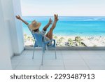 Small photo of Young woman relaxing in chair on balcony of beachfront hotel or apartment.