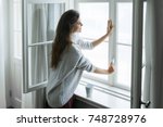 Woman is opening window to look at beautiful snowy landscape outside