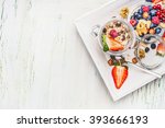 Healthy breakfast preparation: Muesli in jar with summer fresh berries, seeds and  nuts on light wooden background, top view,place for text