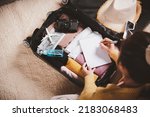 Small photo of Making check list of things to pack for travel. Woman writing paper take note and packing suitcase to vacation writing paper list sitting on room, prepare clothes into luggage, Travel vacation travel